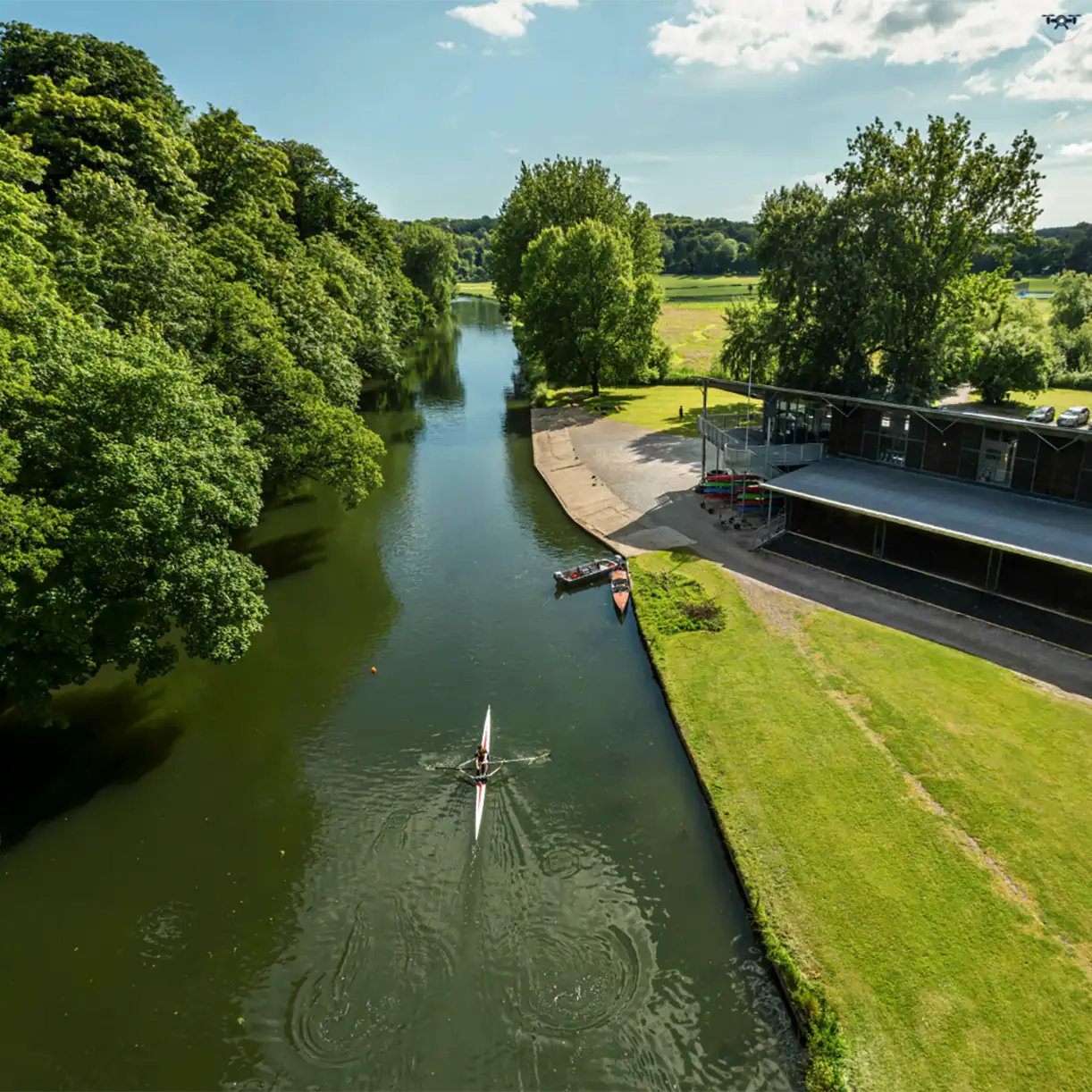 Rowing on river by boathouse aerial